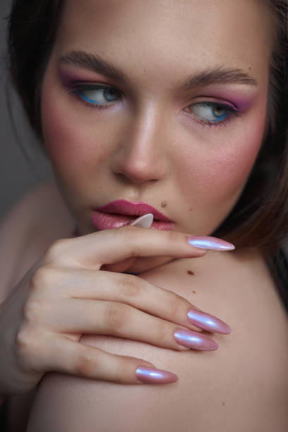 istock model displays stunning long nails with a shiny finish, complemented by colorful eye makeup and soft blush. Her pose highlights the artistry of her manicure and makeup 2185355459