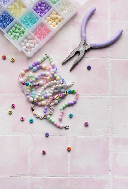 Colorful beads and jewelry making tools arranged on pink tile surface