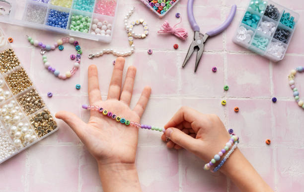 istock Child making beaded bracelets at home on pink tiled table 2185355944
