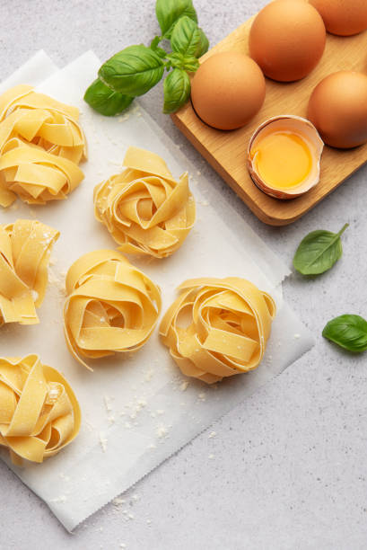 istock Fresh tagliatelle pasta nests with eggs and basil leaves on baking paper 2185356840