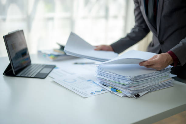 istock A man is sitting at a desk with a laptop and a stack of papers 2185363639