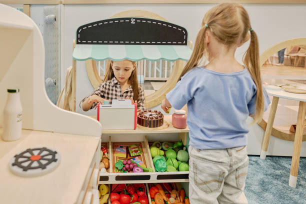 Rear view of little buyer with ponytails standing in front of market stand with clerk holding drink while serving friend