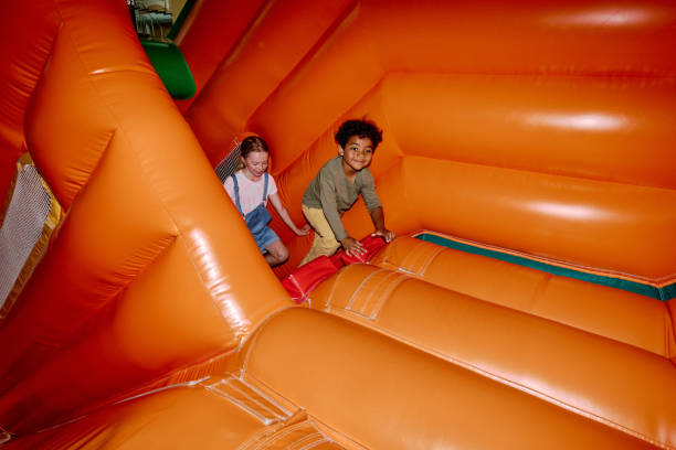 Intercultural friendly children climbing red stairs in soft orange leather tunnel while moving to steep slide