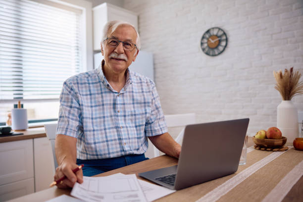 Smiling senior going through his home budget and looking at camera.