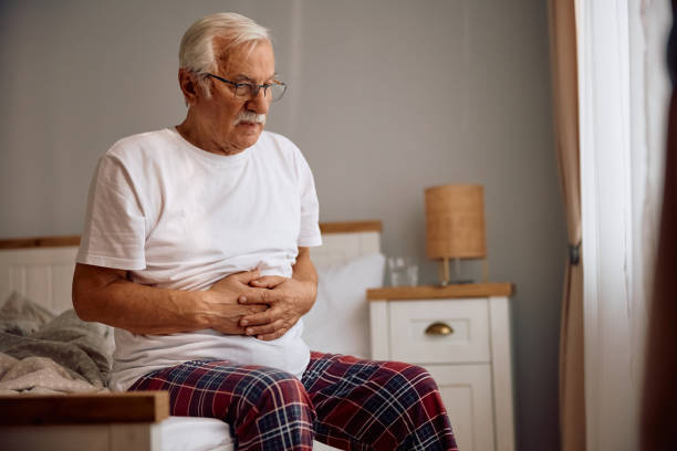 istock Senior man holding his abdomen in pain while sitting on a bed. 2185369126