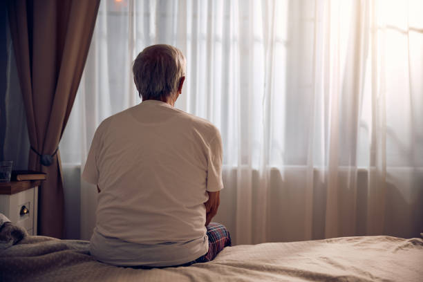 istock Back view of lonely elderly man sitting on a bed at home. 2185369196