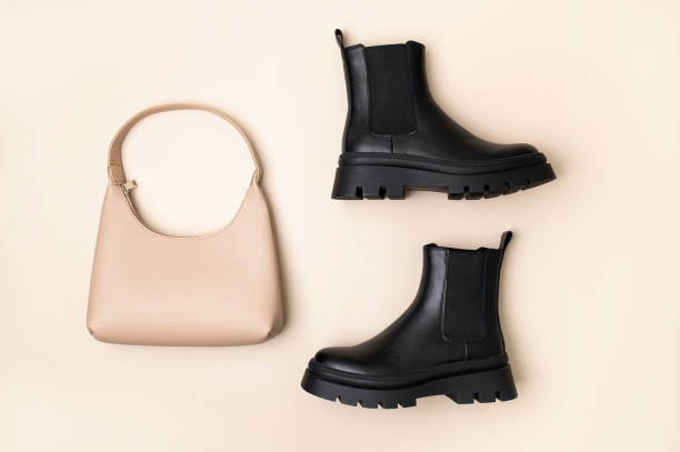 istock Women's black leather boots and leather beige baguette bag on plain beige background top view flat lay. Minimalistic simple background with female accessories 2185370046