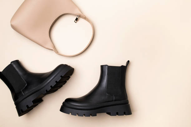 istock Women's black leather boots and leather beige baguette bag on plain beige background top view flat lay. Minimalistic simple background with female accessories 2185370053