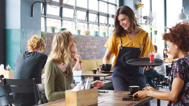istock Two Young Friends Sitting At Table In Coffee Shop Being Given Drinks By Female Server 2185374391