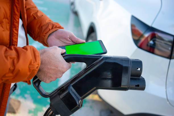 smart phone with green screen and charging dock are in male hand on foreground focus on foreground car is background horizontal still stock photo