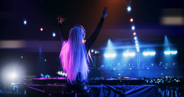 istock Female DJ Delivers a Live Performance of Electronic Music while Standing Behind Mixing Decks at a Massive Event. Colorful Lights and Dance Beats Play at an EDM Concert. Back View 2185377910
