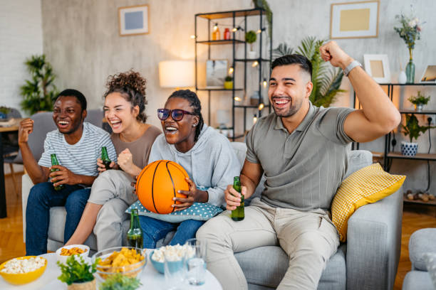 istock Group Of Friends Drinking Beer And Having Snacks While Watching A Basketball Game Together In The Living Room 2185378043