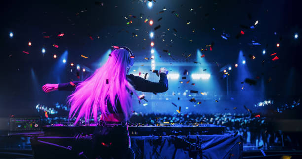 istock Female DJ Delivers a Live Performance of Electronic Music while Standing Behind Turntable Decks at a Massive Concert. Dance Beats Play at an EDM Concert with Falling Confetti. Footage from the Back 2185378066