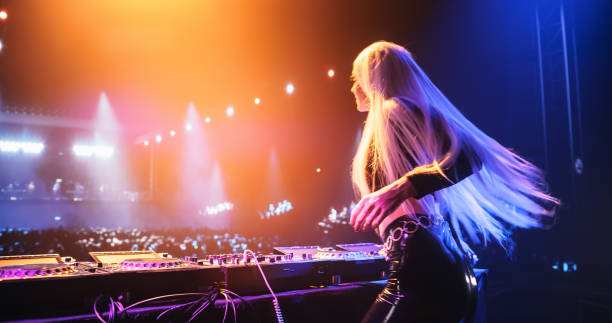 istock Female DJ Delivers a Live Performance of Electronic Music while Standing Behind Mixing Decks at a Massive Event. Colorful Lights and Dance Beats Play at an EDM Concert. Back View 2185378800