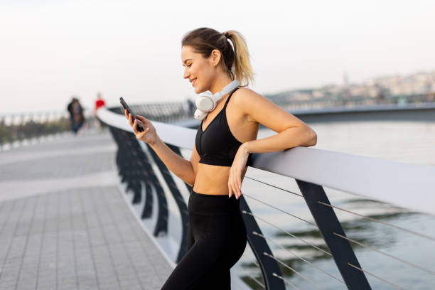 istock Young woman enjoying a call while taking a break from her jog at a tranquil riverside promenade during a sunny afternoon 2185379841