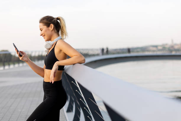 istock Young woman enjoying a call while taking a break from her jog at a tranquil riverside promenade during a sunny afternoon 2185379878