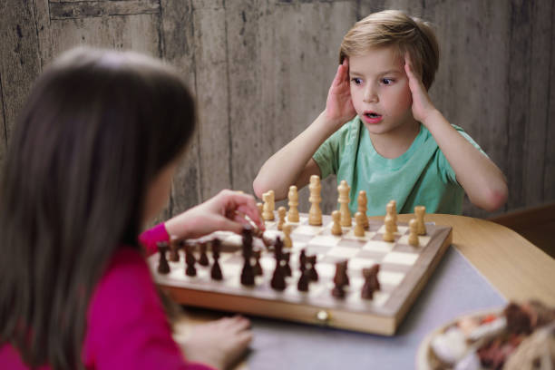 A boy loses a game of chess while playing with his sister at home