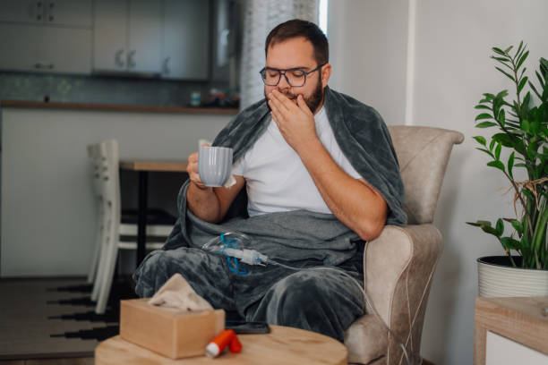 istock Sick man yawning and drinking tea at home while holding a tissue 2185382201
