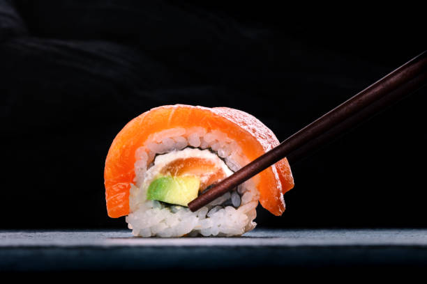 Salmon sushi with avocado and cream cheese, uramaki roll on black