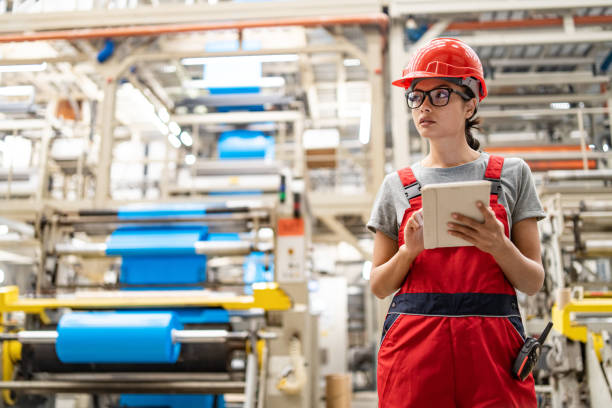 istock Focused female worker checks tablet for processes in expansive modern manufacturing plant. 2185383893