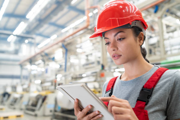 istock Female worker in red protective gear using a tablet in a large factory, focused and precise. 2185383900