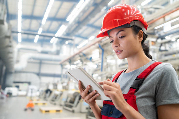 istock Female worker in red protective gear using a tablet in a large factory, focused and precise. 2185383901