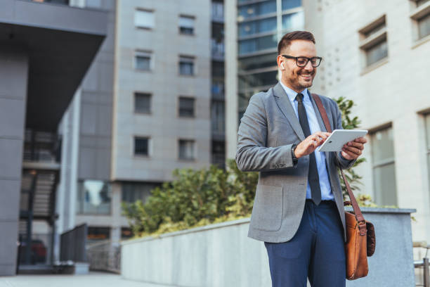 istock Smiling Businessman Using Tablet Outside Modern Office Building 2185384004