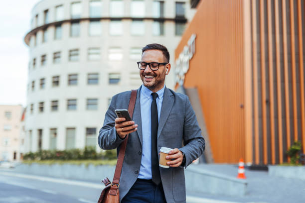istock Smiling Businessman Checking Phone While Walking with Coffee 2185384024