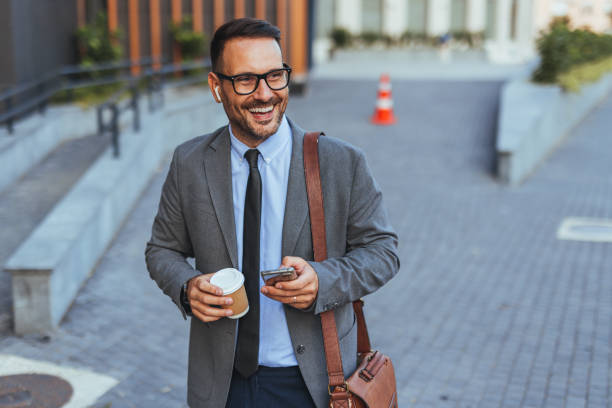 istock Smiling Businessman Walking Outdoors With Coffee and Smartphone 2185384089
