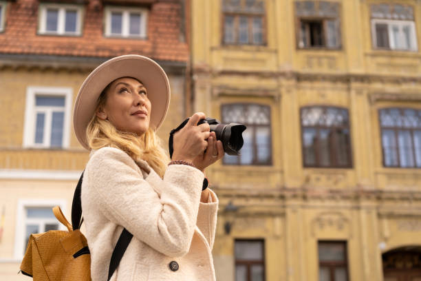 istock Sightseeing woman captures urban architecture with camera, wearing a hat and yellow backpack 2185386403