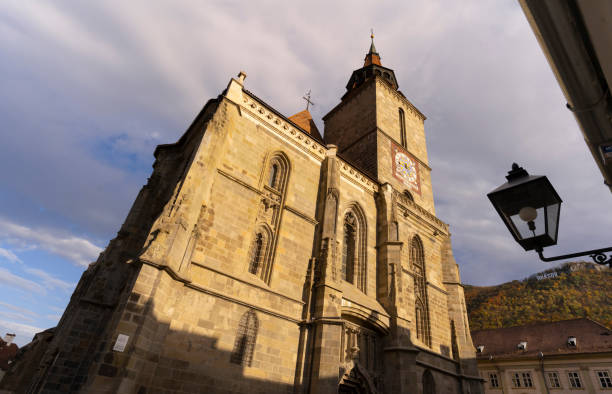 An imposing medieval church stands tall with intricate stone architecture, illuminated by the warm glow of the setting sun under a dynamic sky.