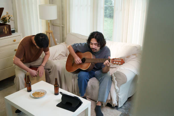 istock Asian playing guitar while his friend plays a cajon, both singing and enjoying a musical jam session in a living room. Friendship concept. 2185390792