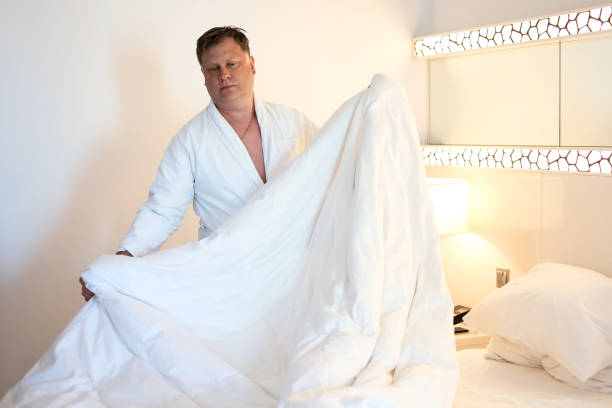 istock Sleep-Deprived Man Struggles to Make His Bed: A Morning Reflection on the Challenges of Restless Nights and the Pursuit of a Fresh Start in Daily Life 2185392553