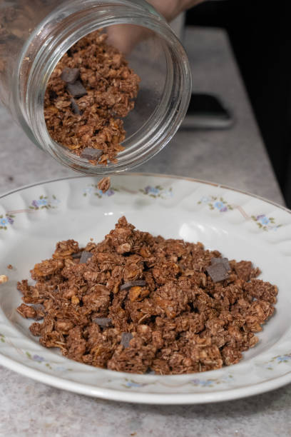 istock Hands pouring cereal with chocolate pieces from a glass jar into a white bowl 2185396415