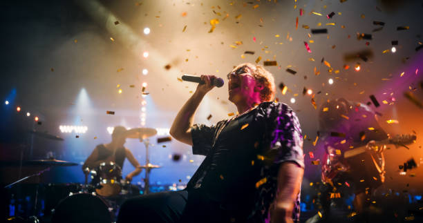 istock Professional Rock Musicians Performing Under Falling Confetti on Festival Stage, Playing Popular Rock Tracks in Front of a Crowded Concert Arena. Electrifying Performance at an Indoors Festival 2185398819