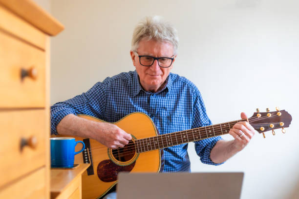 istock Senior man learning to play acoustic guitar by watching online video tutorial on laptop 2185399541