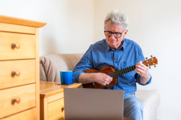 istock Senior man learning to play ukulele by watching online video tutorial on laptop 2185399542