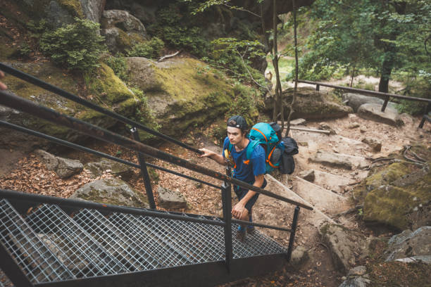 istock Hiker with a blue backpack carefully ascends metal stairs surrounded by moss-covered rocks and dense greenery, navigating a rugged forest trail in the Beskydy Mountains 2185401282