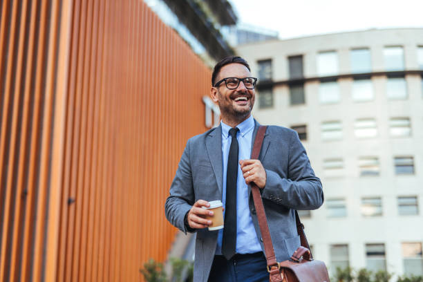 istock Smiling Businessman Walking with Coffee in Urban Setting 2185403558