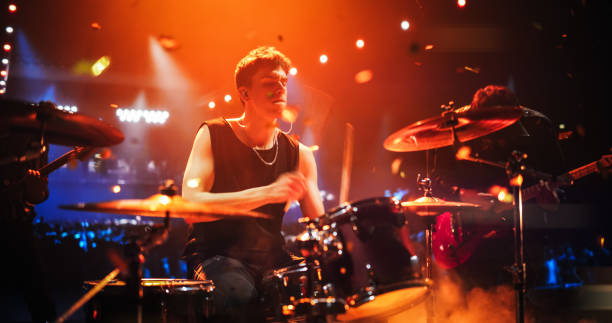 istock Handsome Young Drummer Performing on Concert Stage with His Band Members, Surrounded by Falling Confetti and Pulsating Visuals. Young Musicians Showcasing Their Skills and Energy. Slow Motion Footage 2185404046