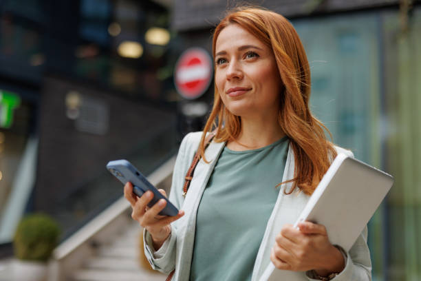 Thoughtful woman stands with technology in urban setting