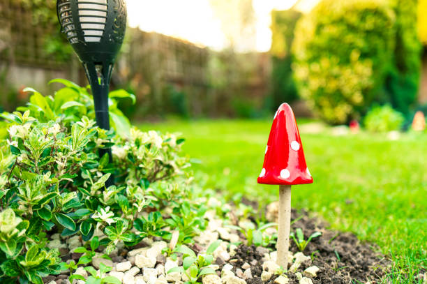 Close-up of a hand painted Toadstool ornament seen in a fresh, springtime flowerbed. A solar light can be seen on the left of the Toadstool.