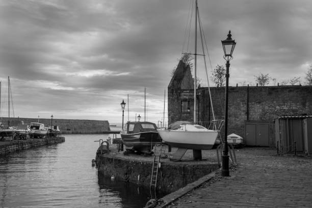 Black and white photo of the harbour at the dusk, roofless stone building, boats, old lantern