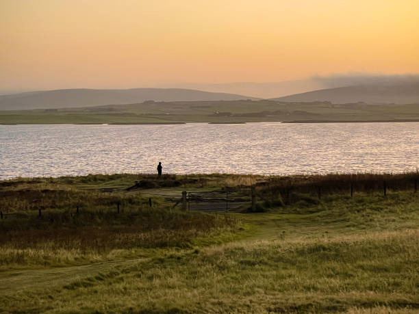 Solitary individual looking over Loch of Harray, just before dawn, in the Orkney Islands of Scotland.