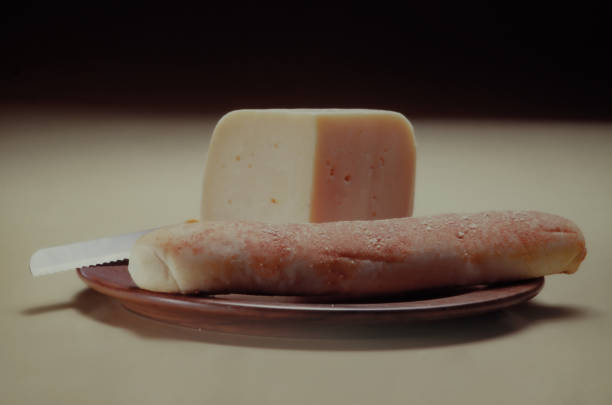 A large piece of cheddar cheese next to a delicious baguette on a wooden board.