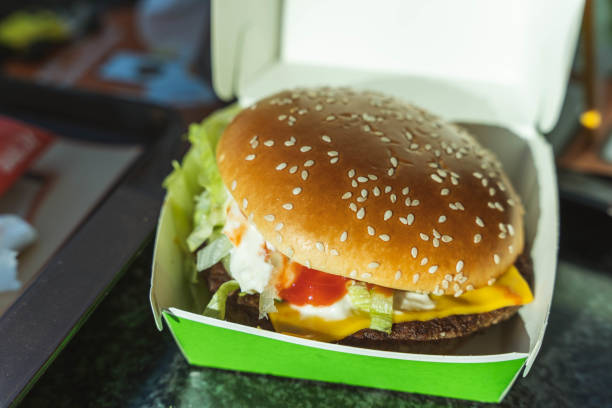 A mouth-watering, tempting, and juicy burger is presented in a paper box on a cozy cafe table, creating a warm and inviting atmosphere that makes you crave for a delightful meal.