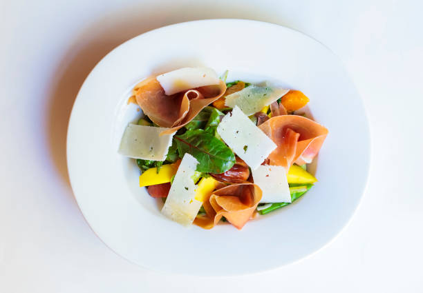 Fresh salad with assorted greens, mango, and cured meats served in a white bowl