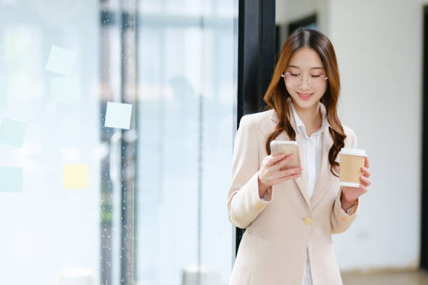 istock Businesswoman smiling while holding a coffee cup and checking her phone during a work break 2185420282