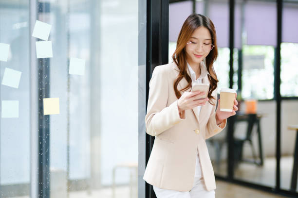 istock Businesswoman smiling while holding a coffee cup and checking her phone during a work break 2185420284
