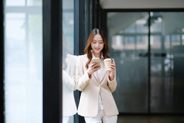 istock Businesswoman smiling while holding a coffee cup and checking her phone during a work break 2185420285